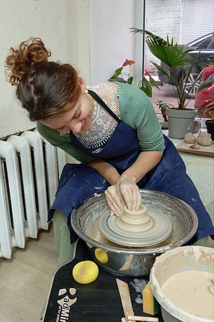 potter is throwing a ceramic vase wearing a linen apron with a split leg feature.