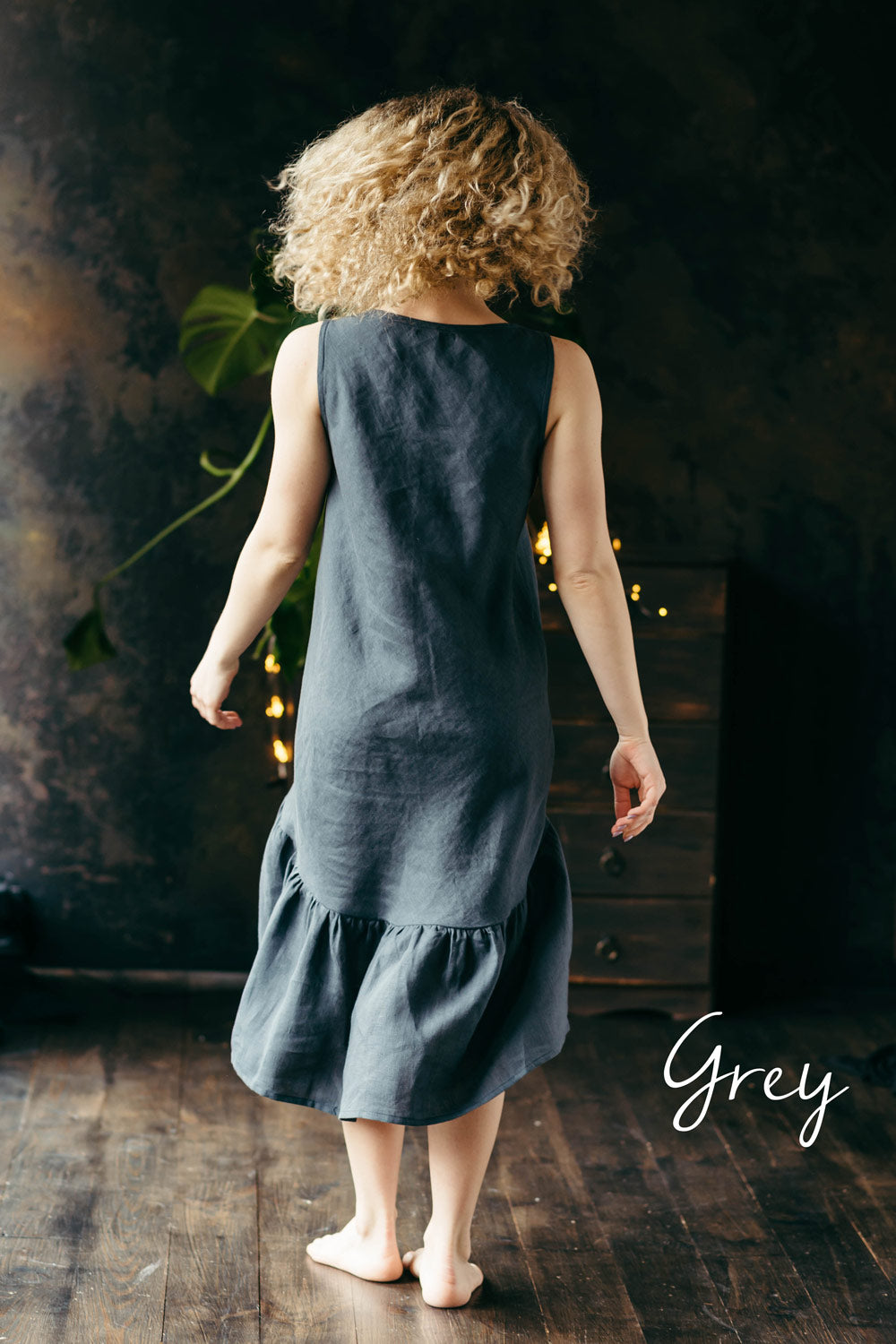 Woman wearing a dark grey linen midi dress standing in a dimly lit room.