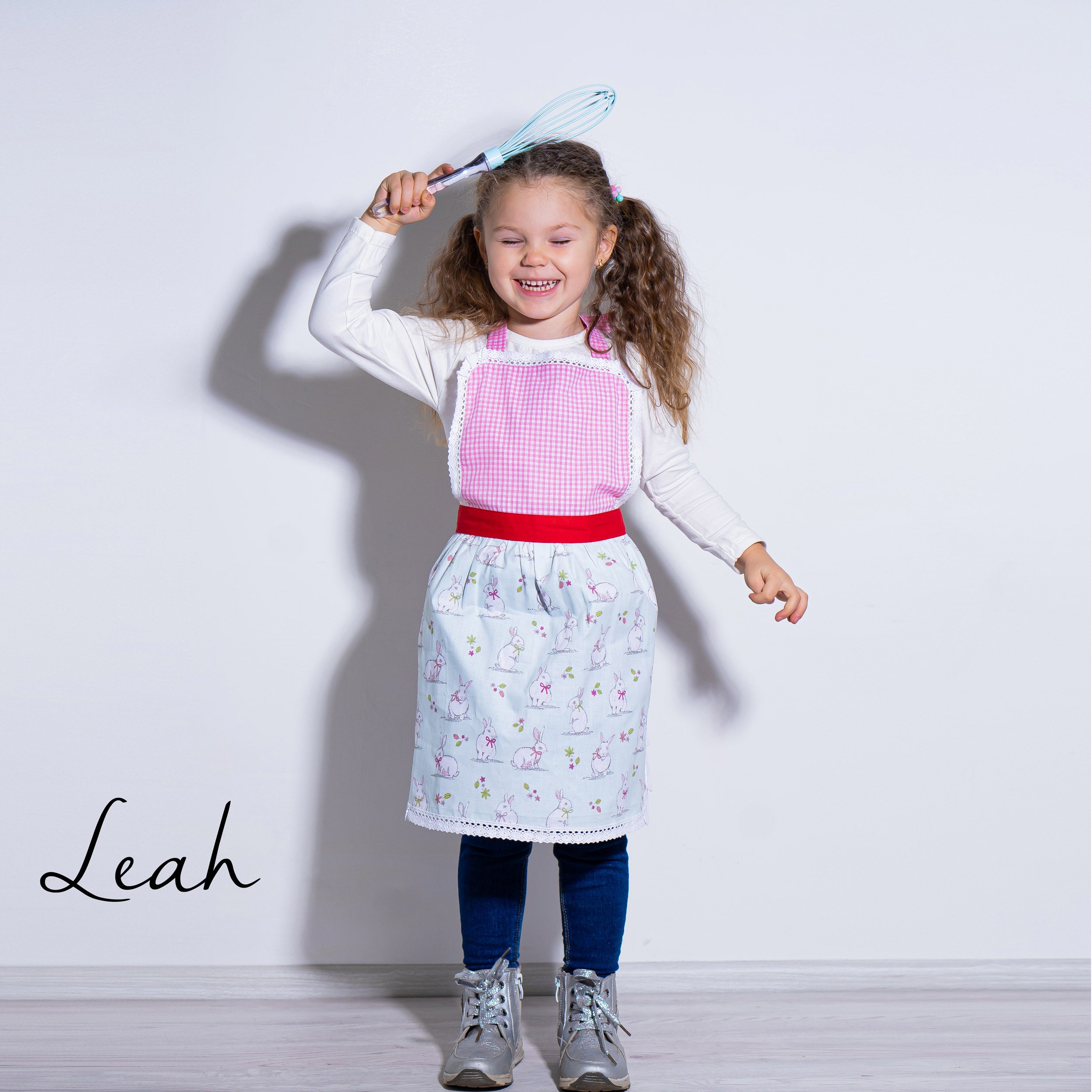 Child wearing a cotton kids aprons with a bunny rabbit print, holding a toy whisk.