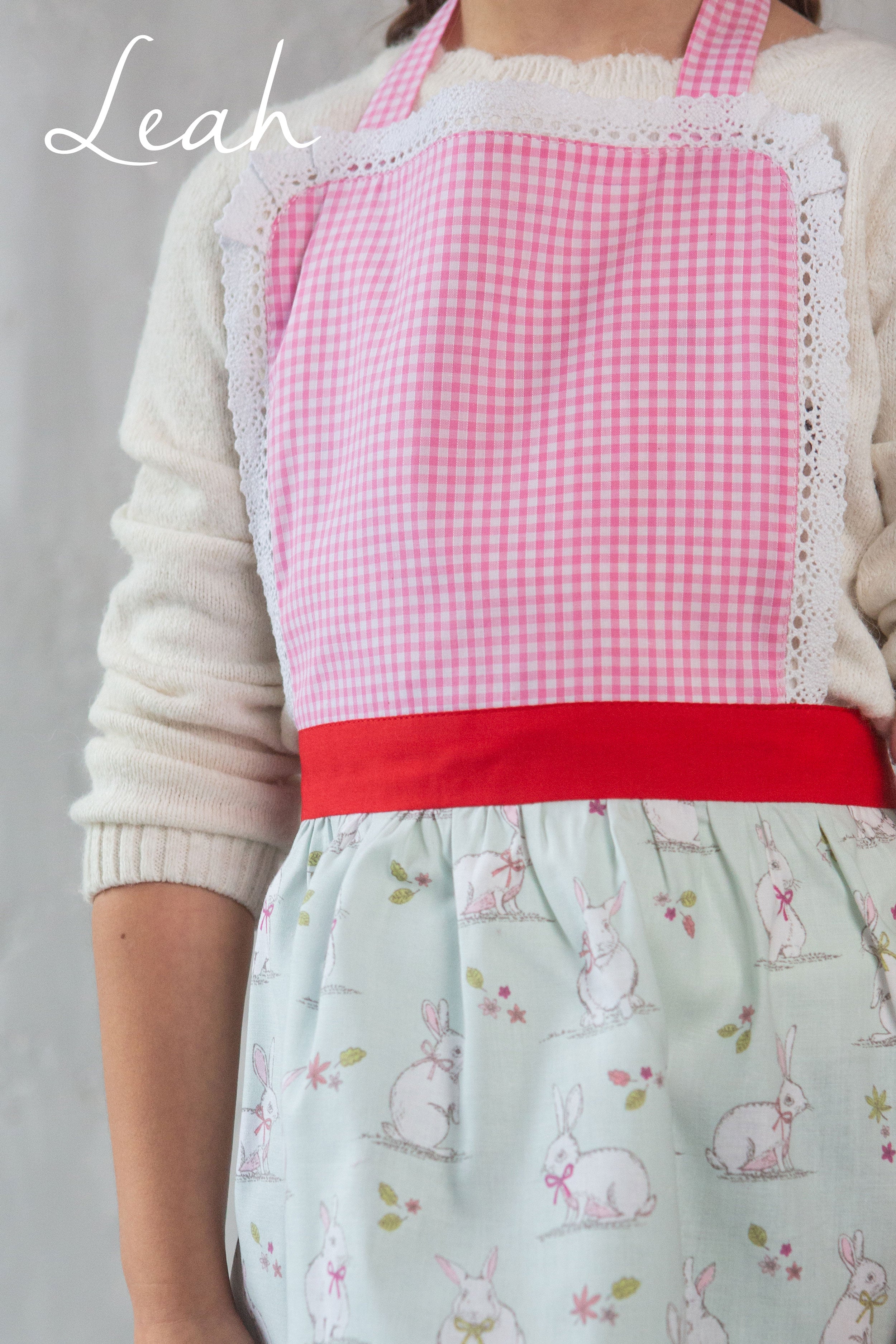 Girl wearing a pink checkered handmade in the UK apron over a light green apron with bunny patterns.
