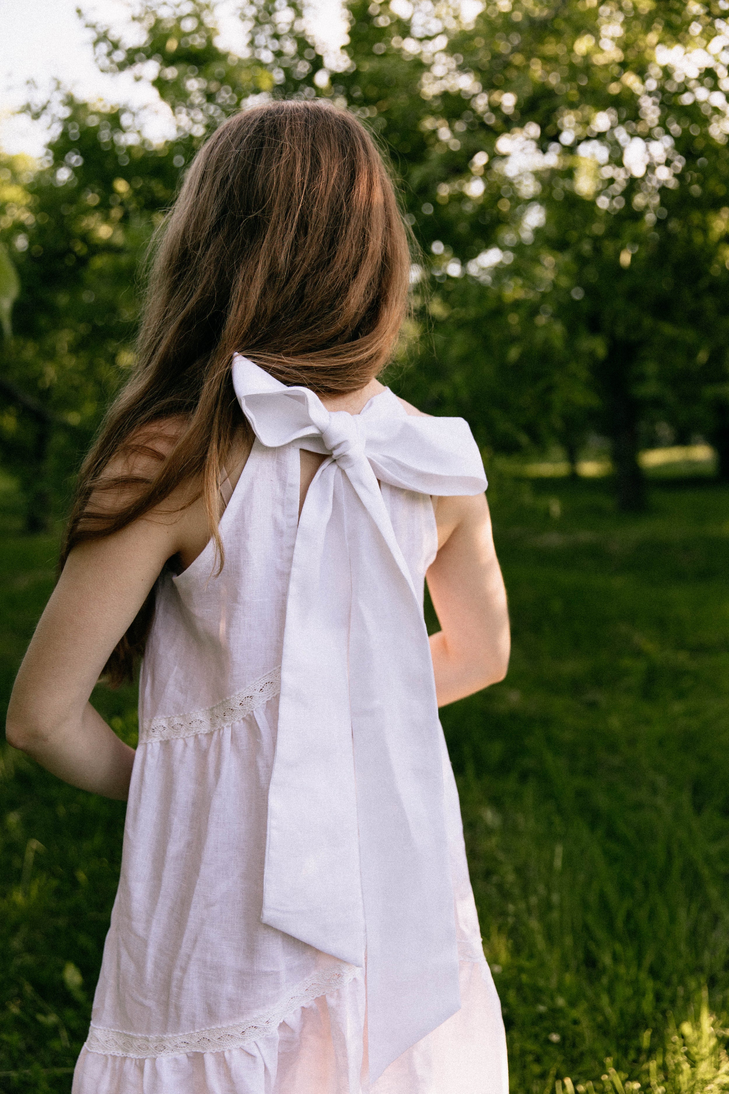 Woman in a white linen wedding dress with a bow standing in a grassy field