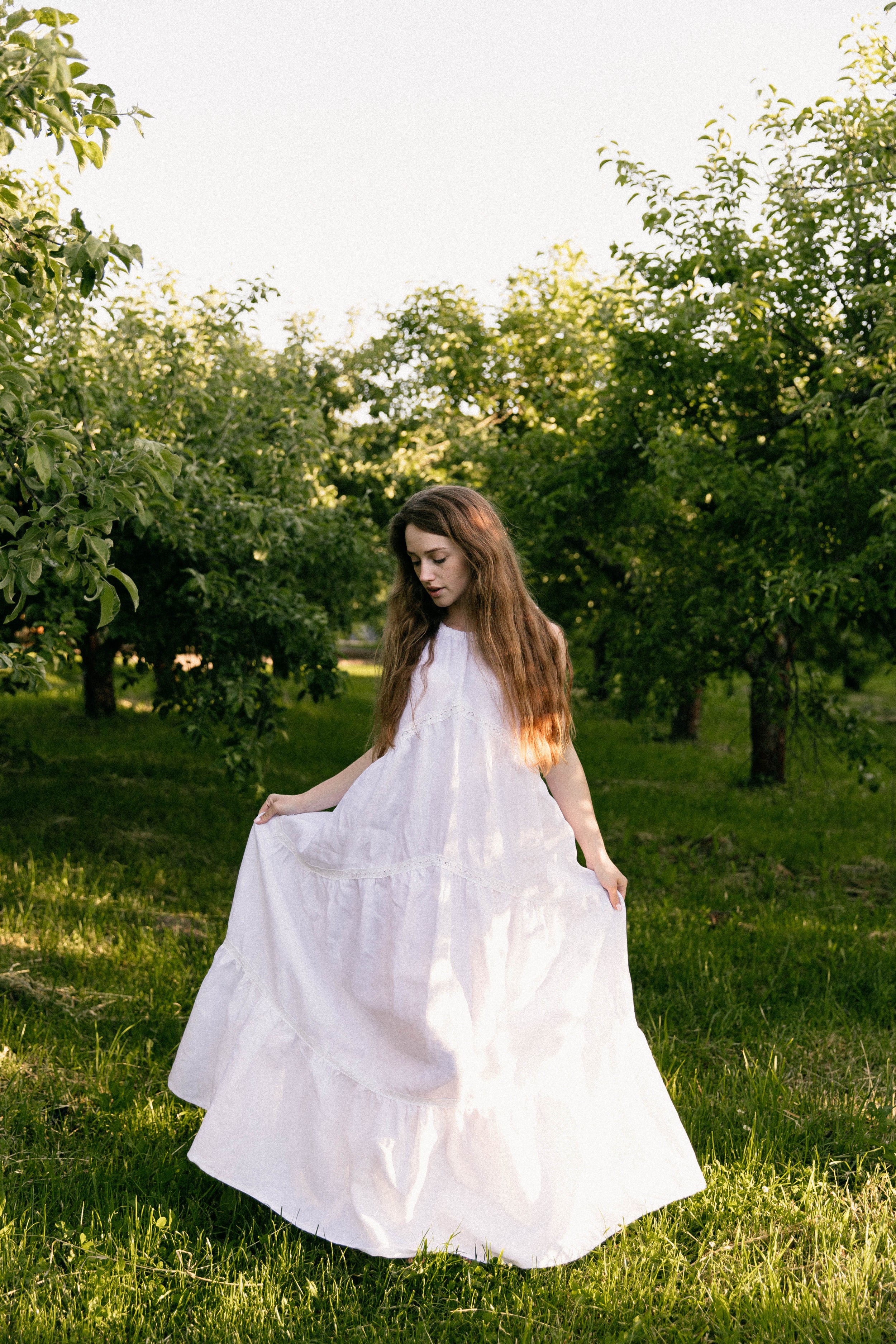 Woman in a white linen wedding dress standing in an orchard