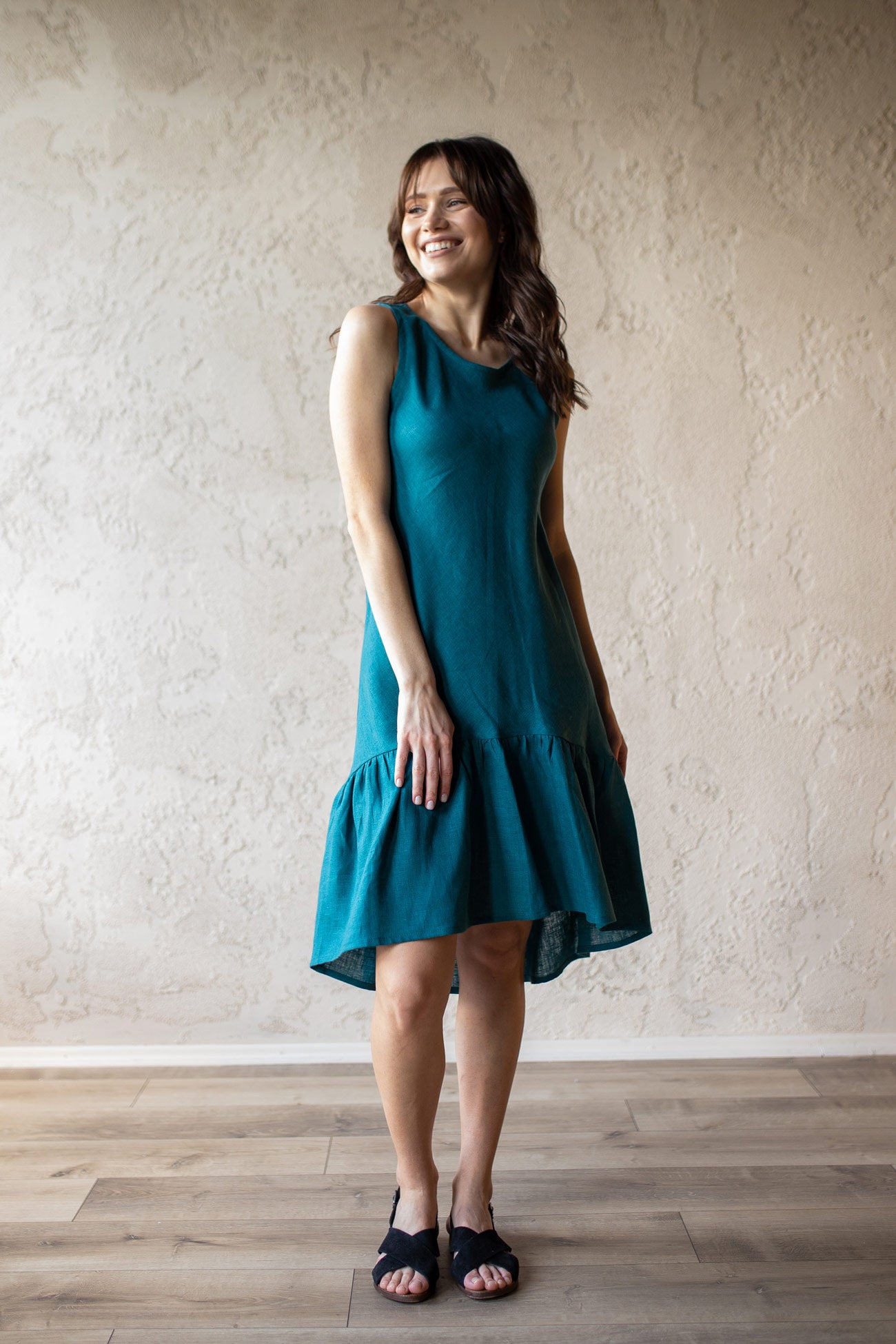 Woman wearing a teal linen summer dress standing against a plain wall.