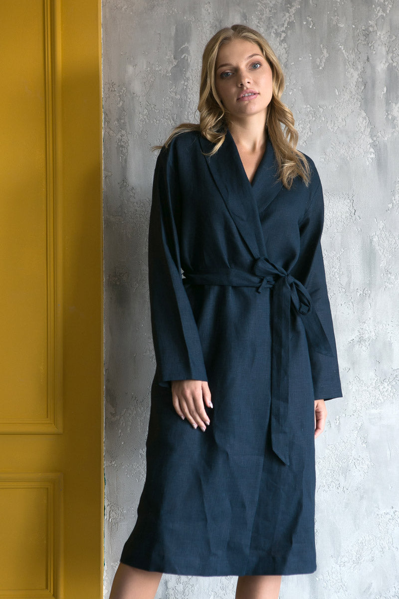 Woman wearing a navy blue natural linen robe against a textured gray wall.