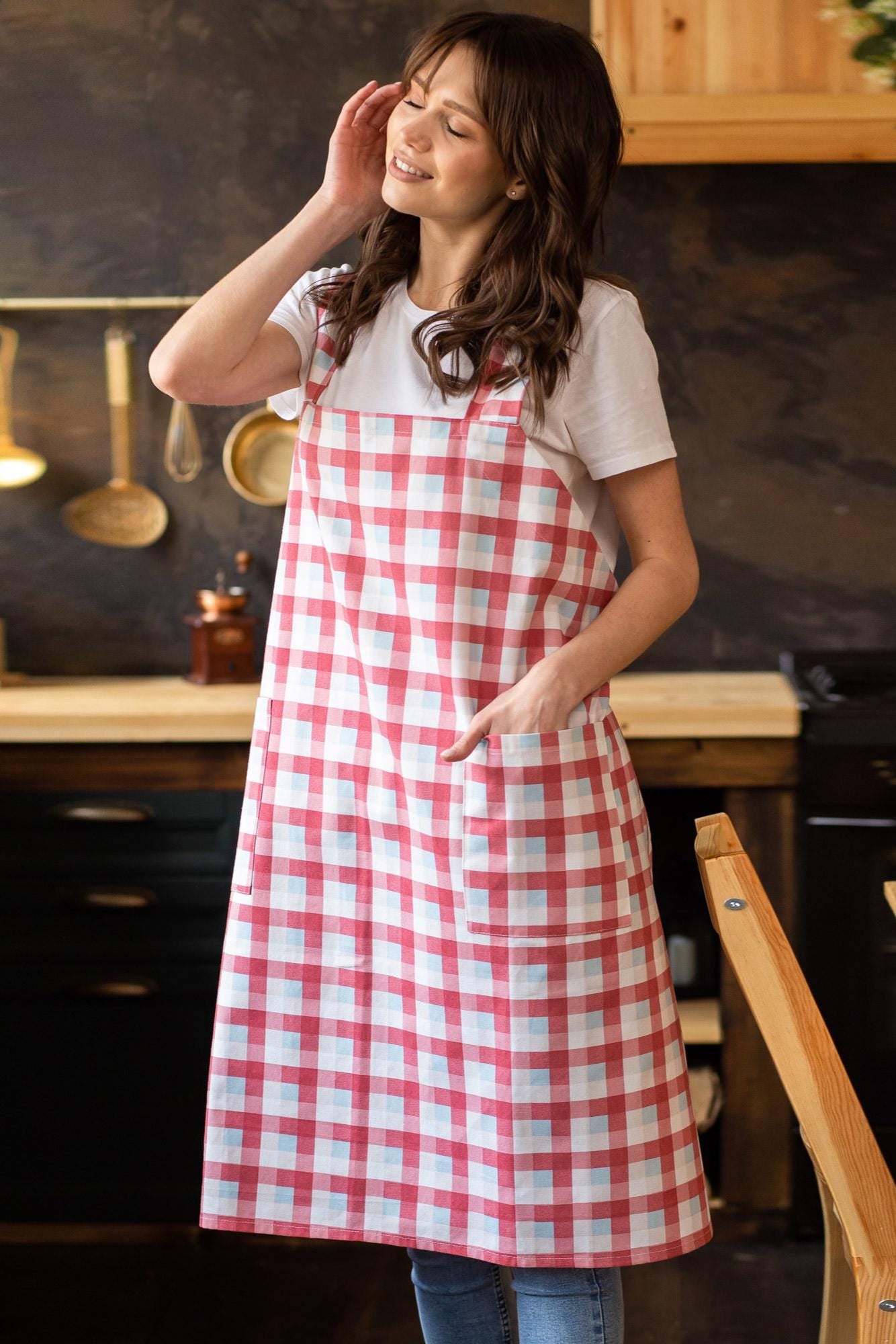 Woman wearing a red and white checkered cross-back pinafore apron in a kitchen.