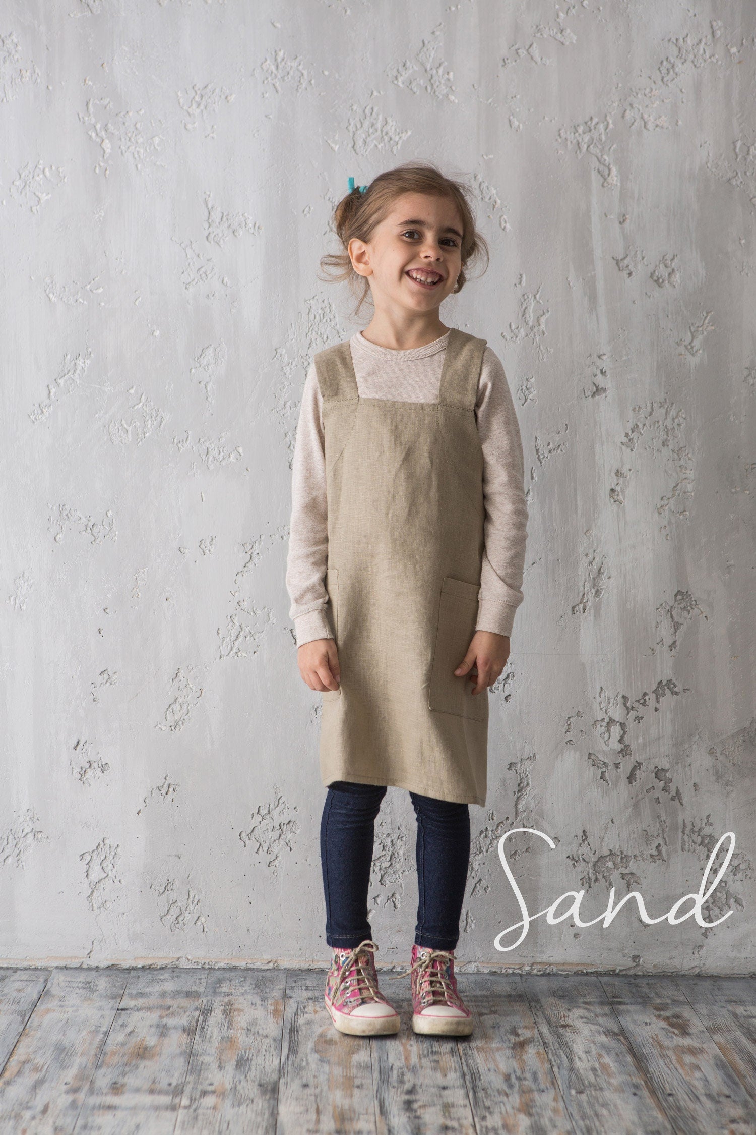 Girl in natural linen pinafore apron standing by wall