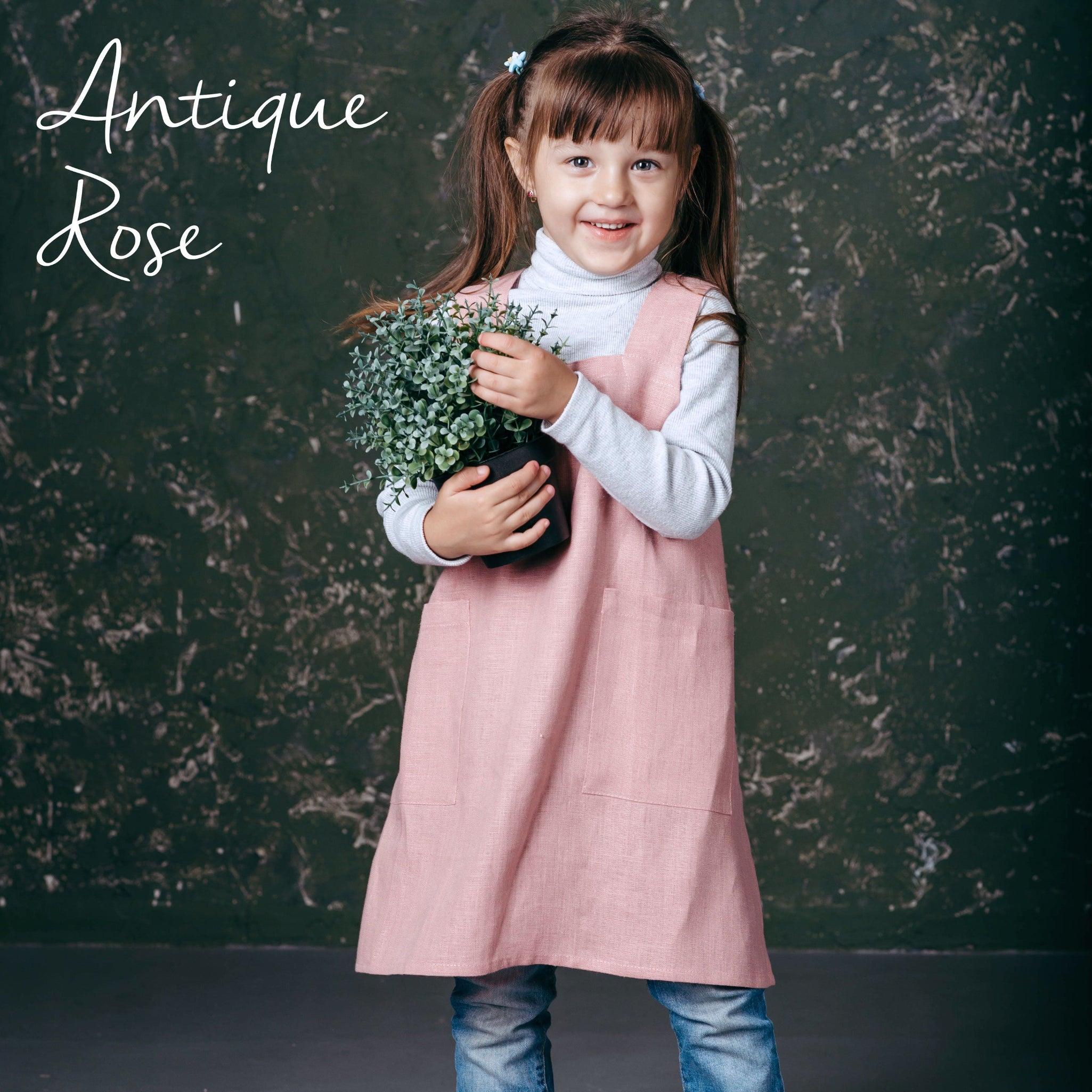 Child in rose pink linen pinafore apron holding flowers