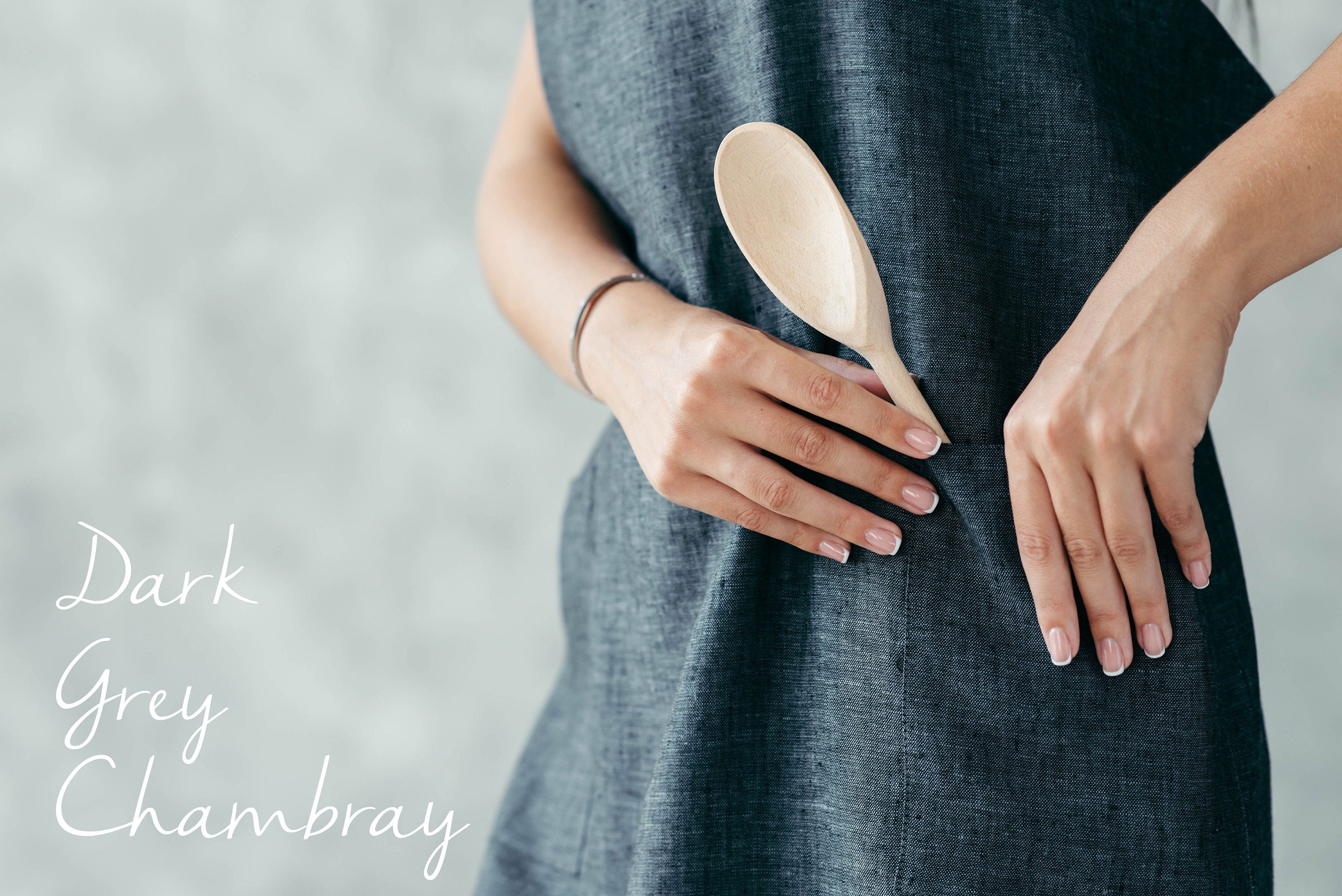Person wearing a dark grey chambray linen apron holding a wooden spoon.