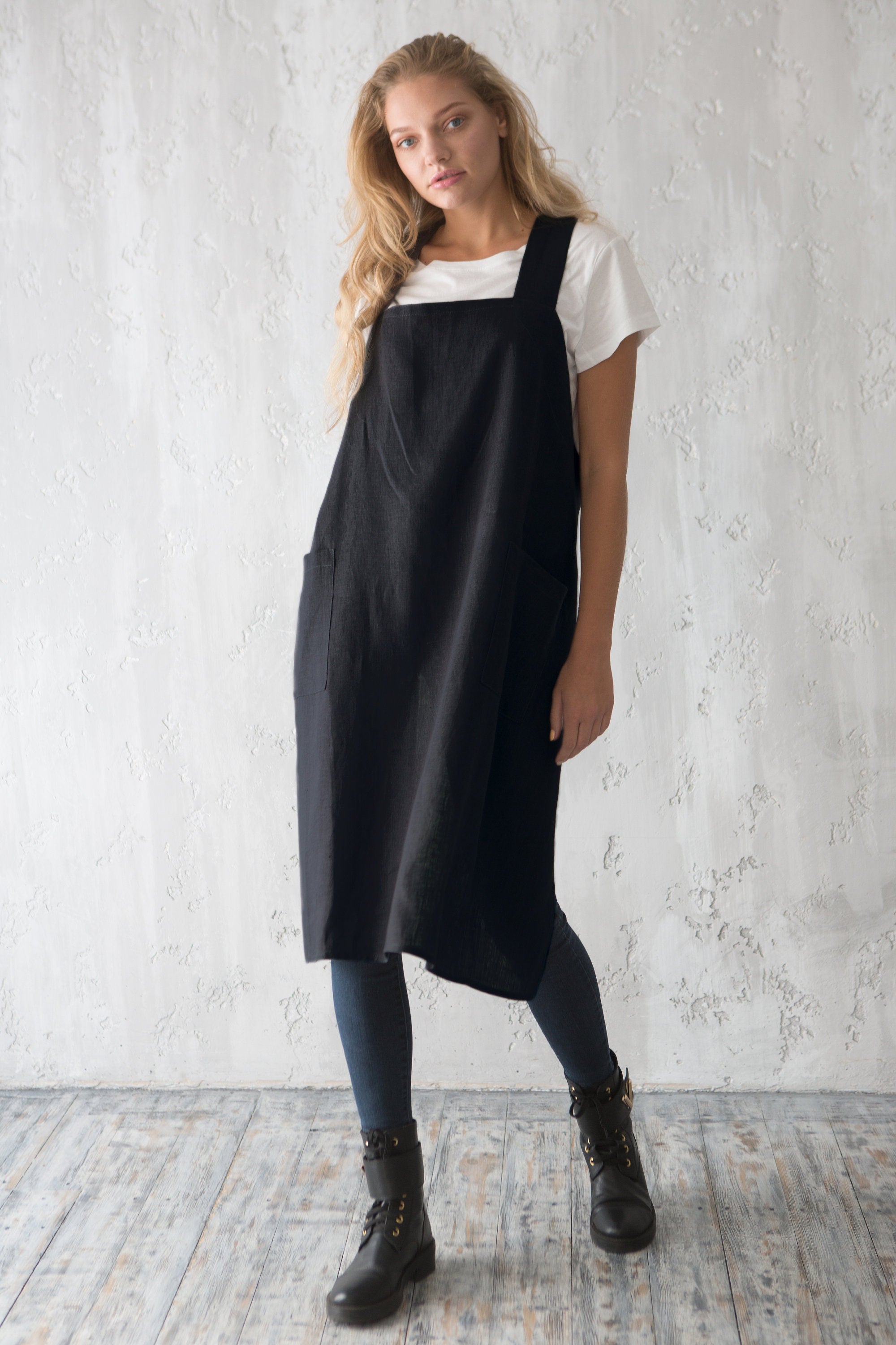 Waitress is wearing a black pinafore apron over a white t-shirt against a light gray wall of a cafe