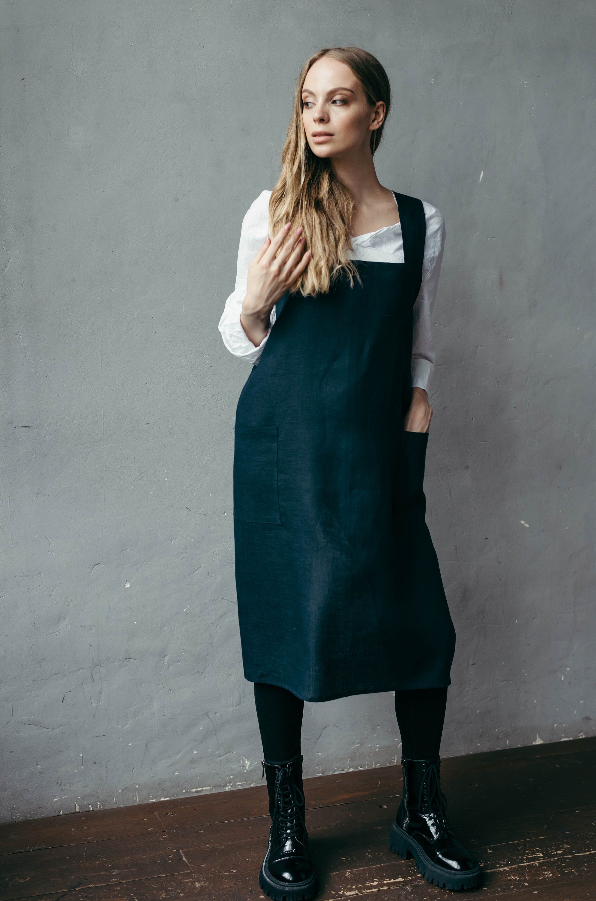 Baker wearing a navy blue apron over a white shirt against a gray wall of her bakery.