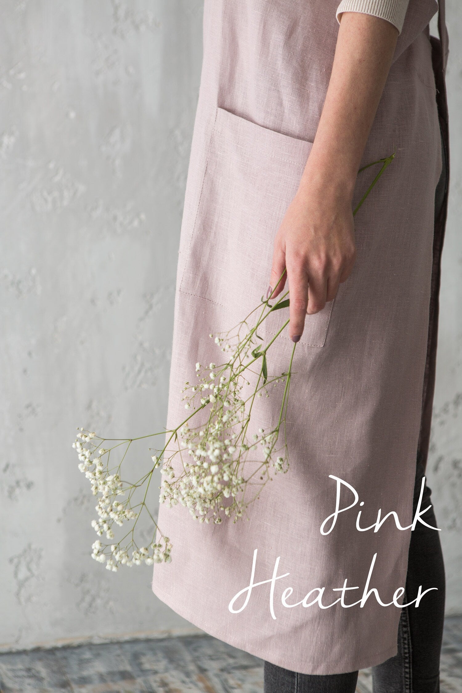Florist wearing a pink heather cross-back linen apron holding flowers.