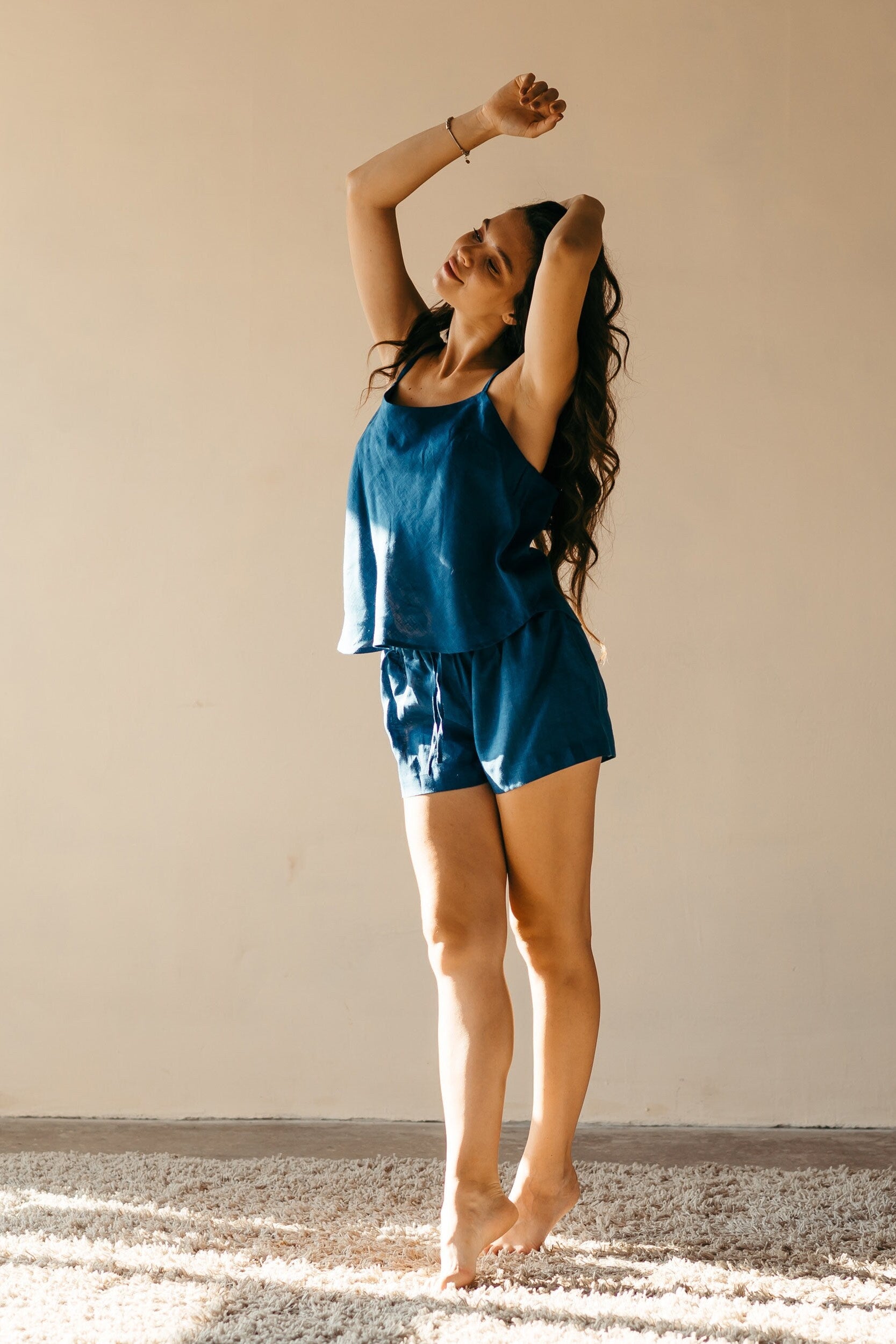Woman in blue pajama set standing with arms raised against a beige wall.