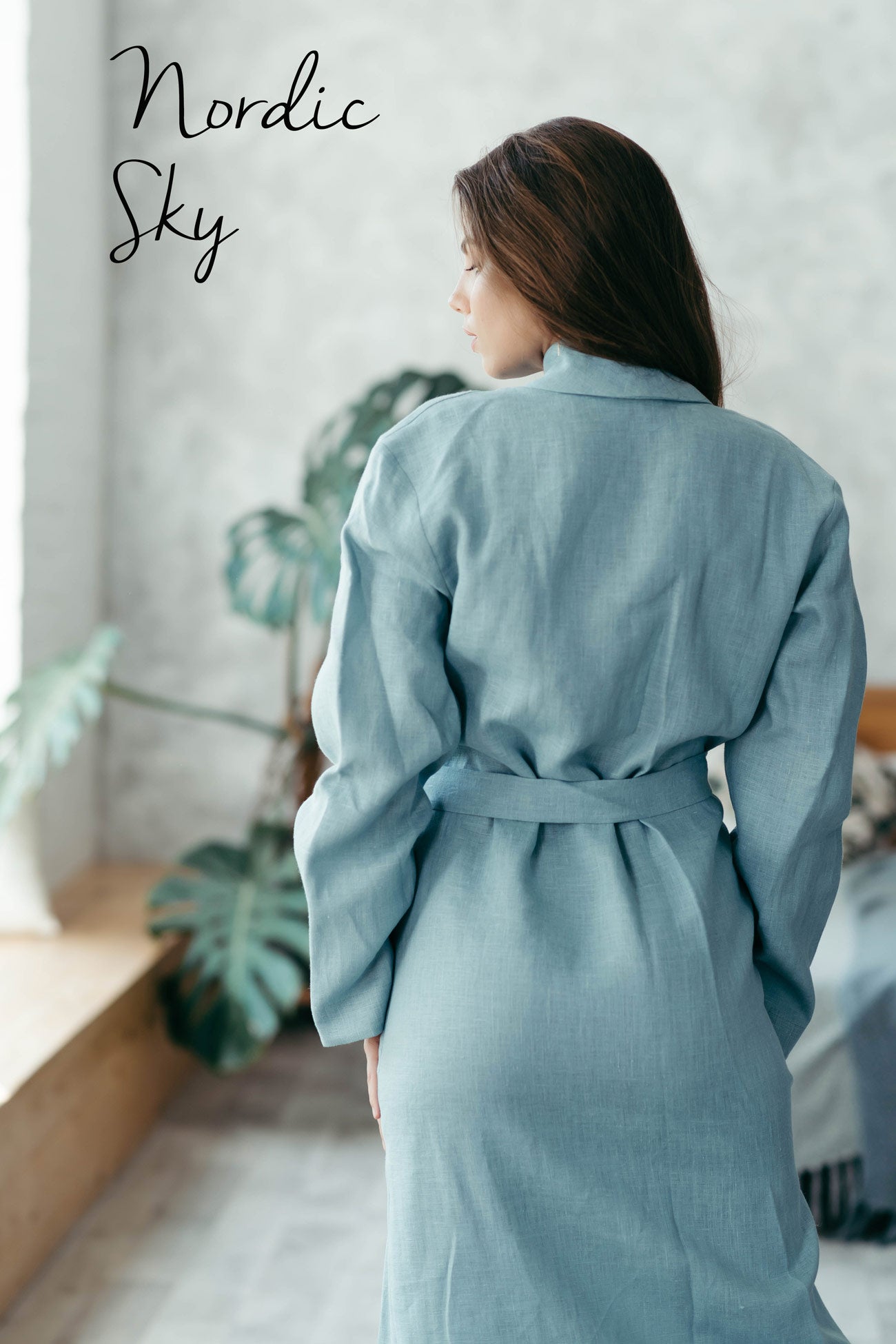 Woman wearing a blue linen robe in a room with plants and a light background