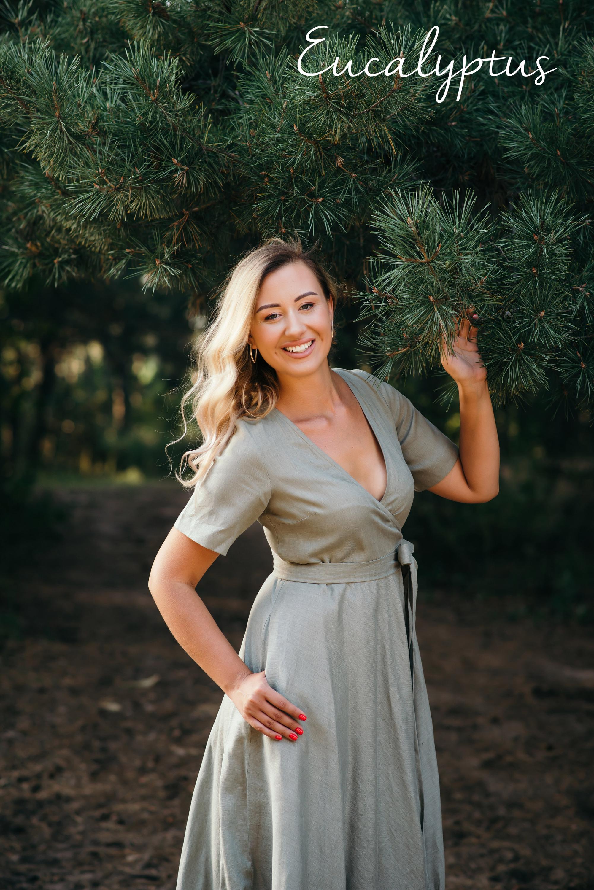 Woman in a light green linen dress standing among eucalyptus trees