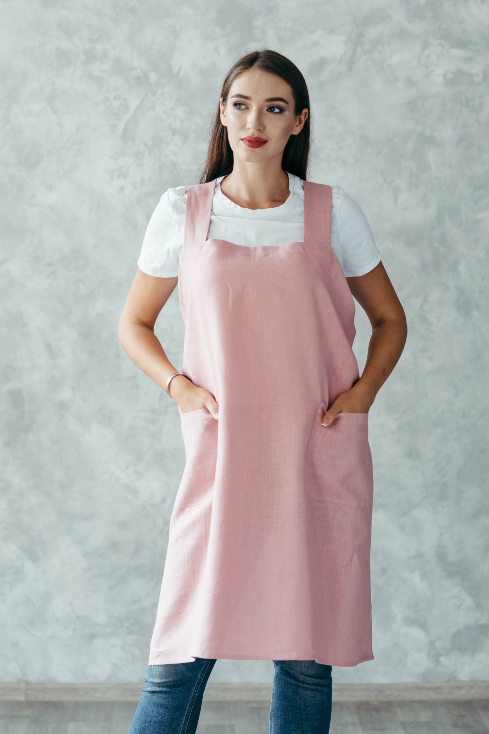 Woman wearing a pink linen pinafore apron against a gray wall
