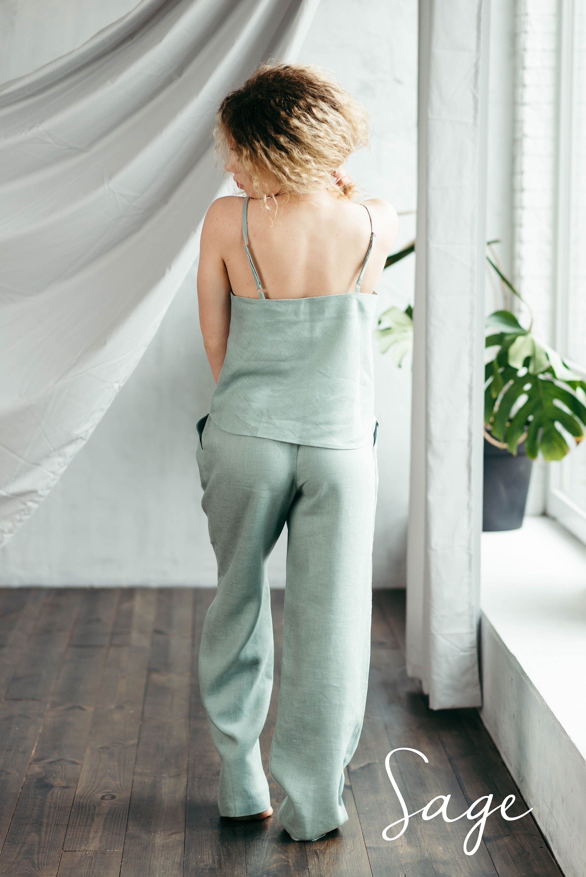 Woman wearing a light turquoise green pajama set standing in a room with white curtains and a plant.
