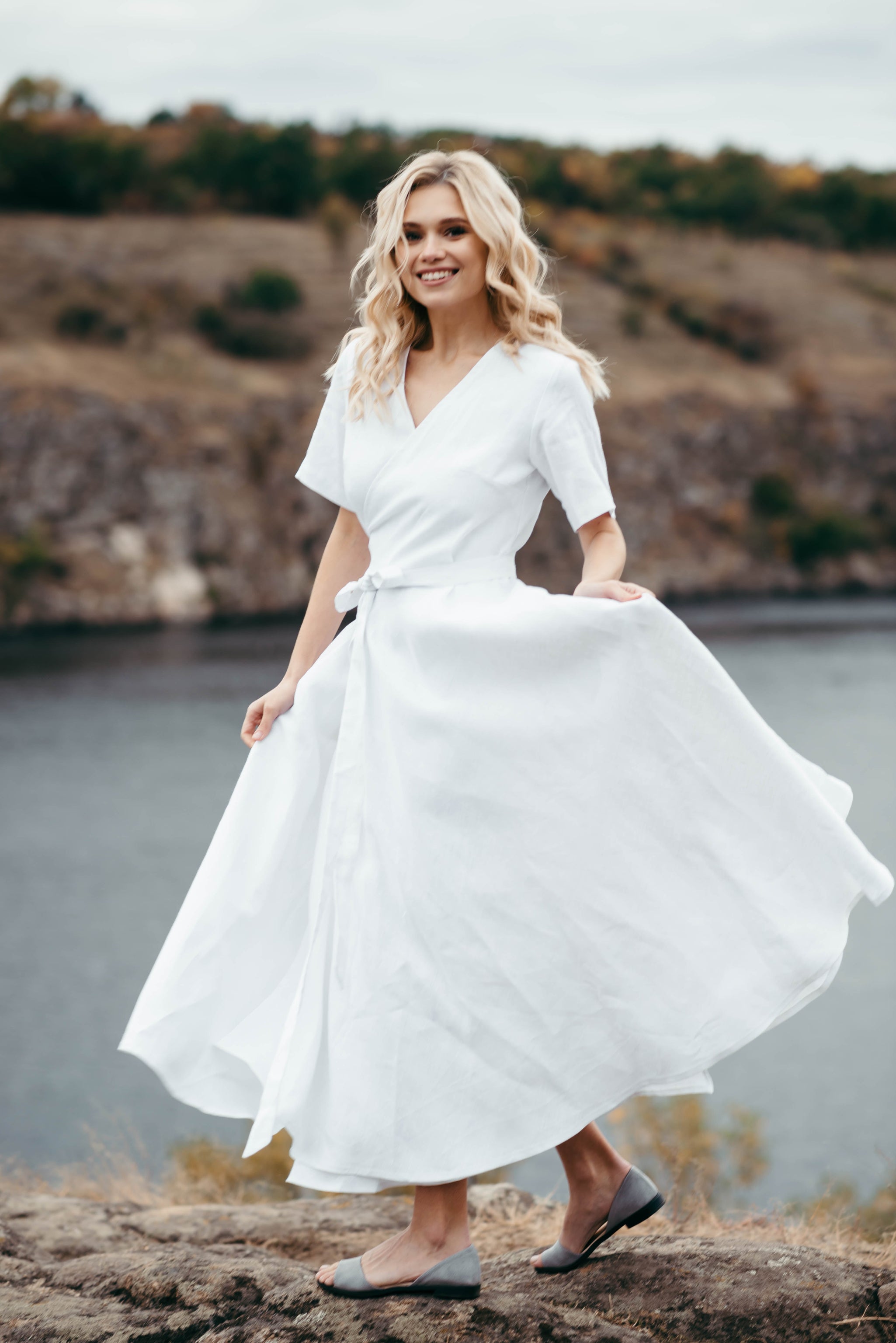 Woman in a simple white linen wedding dress standing by a riverside with a scenic background