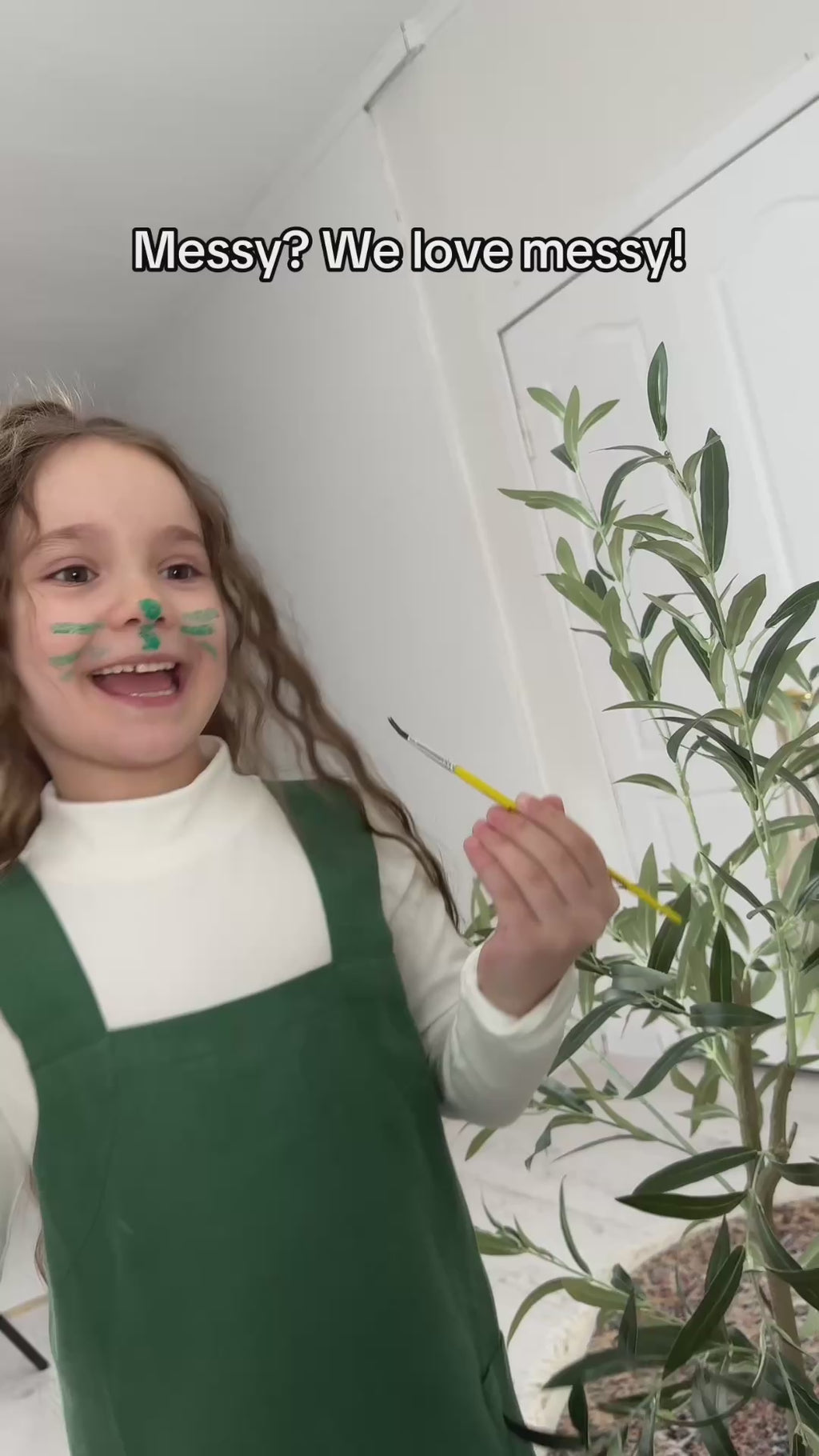 A girl doing face painting in her green linen smock apron for art.