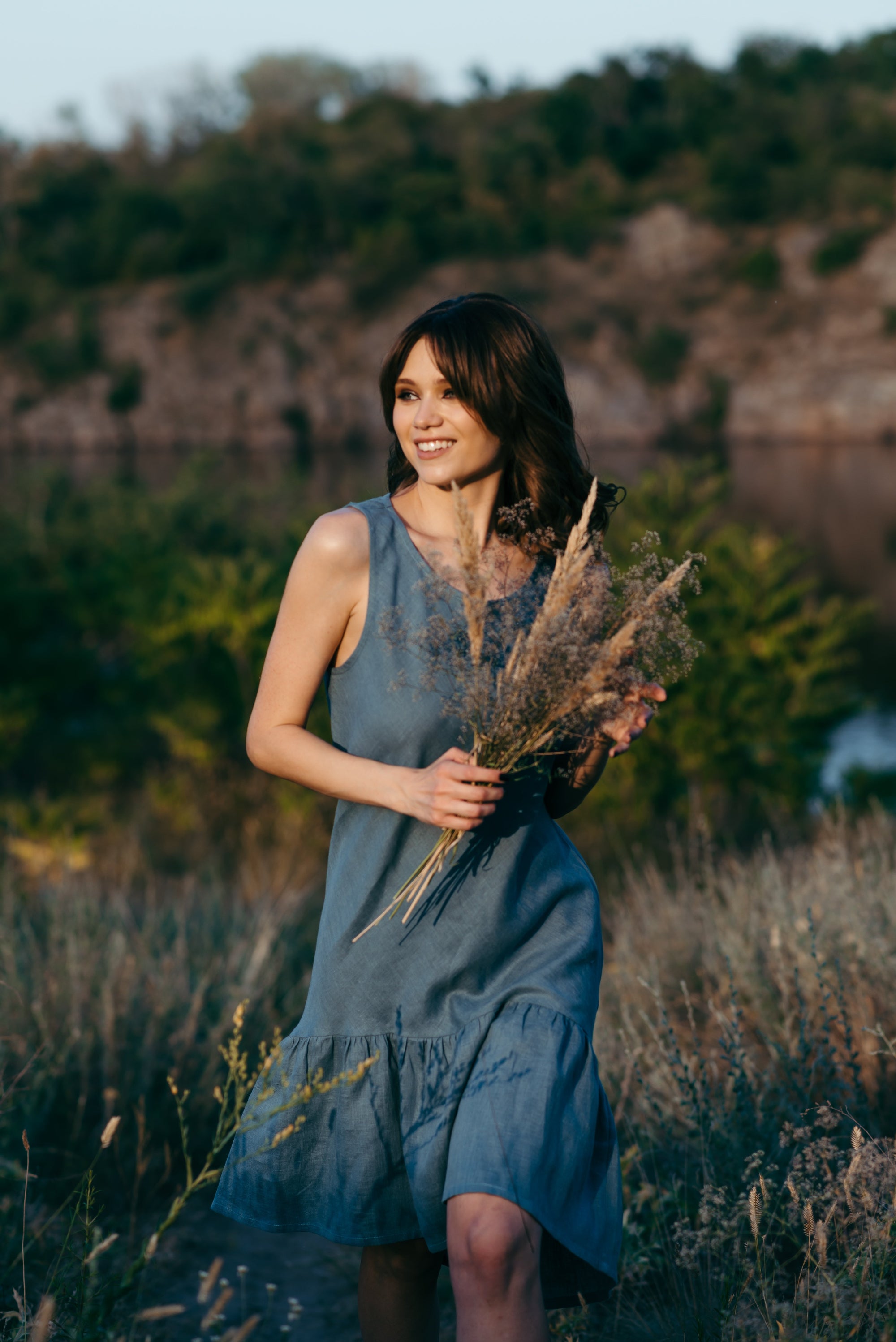Woman in a blue linen summer dress holding dried plants in a natural setting
