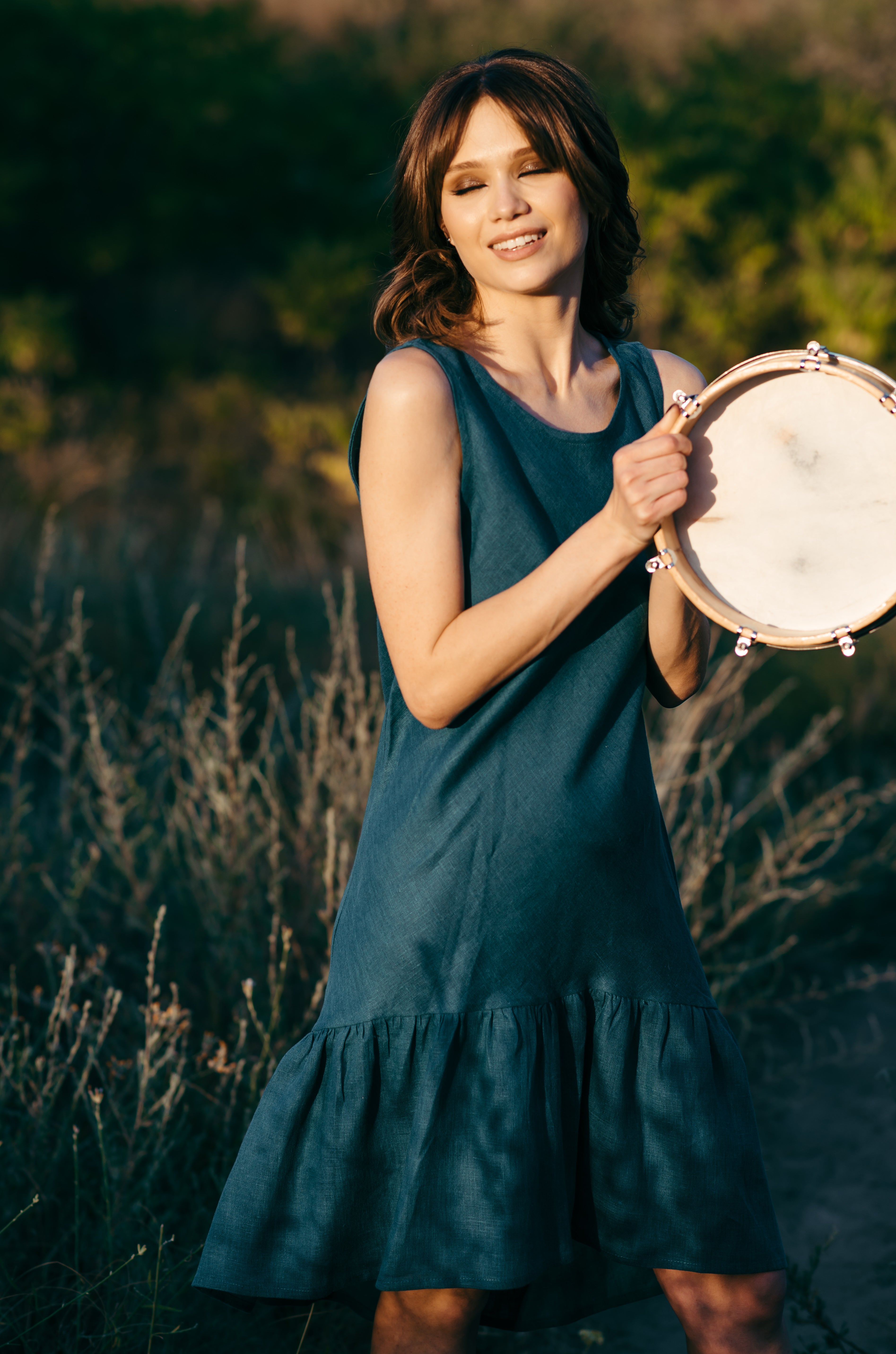 Woman in a turquoise linen midi dress holding a tambourine in a natural setting