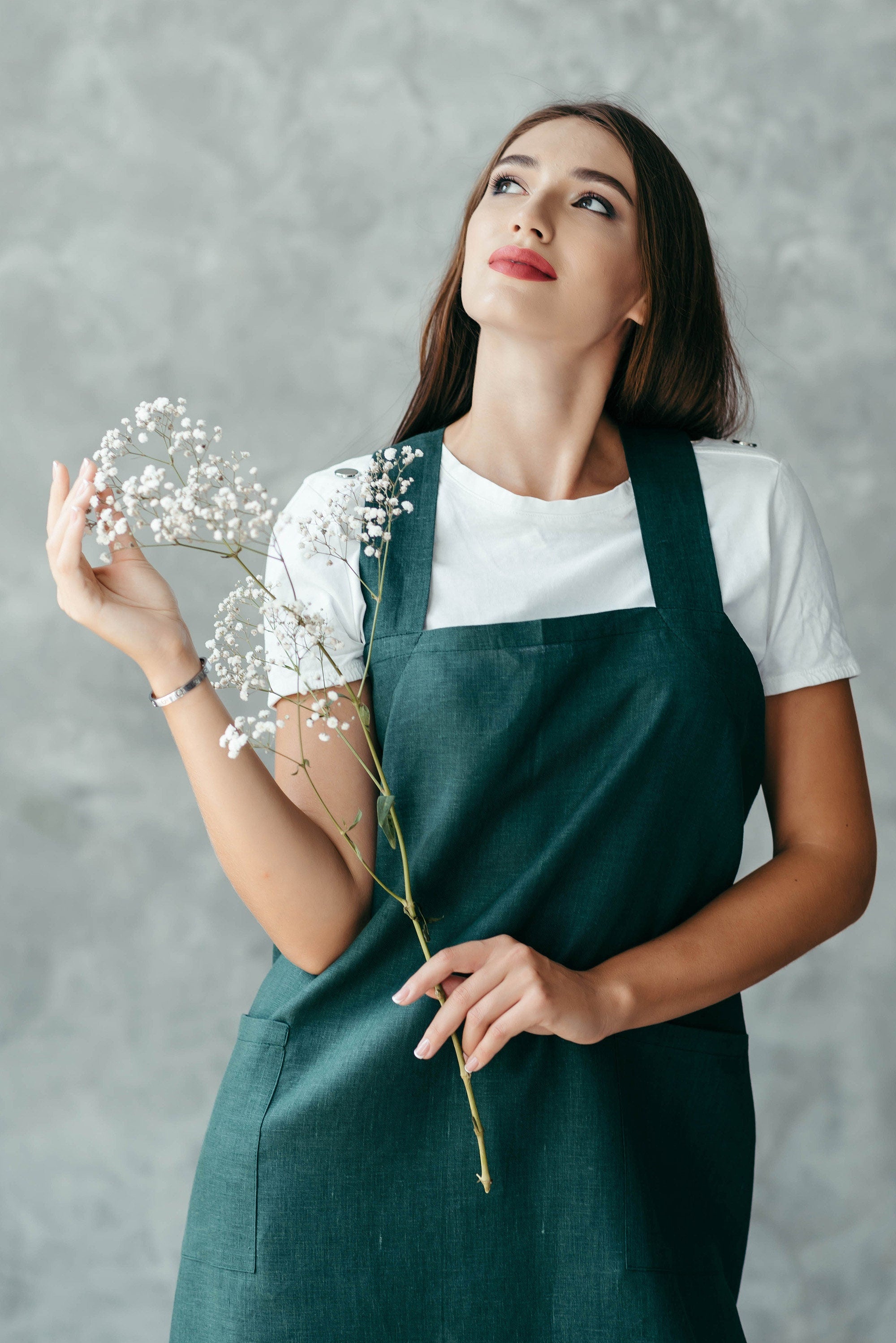 Woman wearing a green apron holding a branch with small white flowers against a gray background