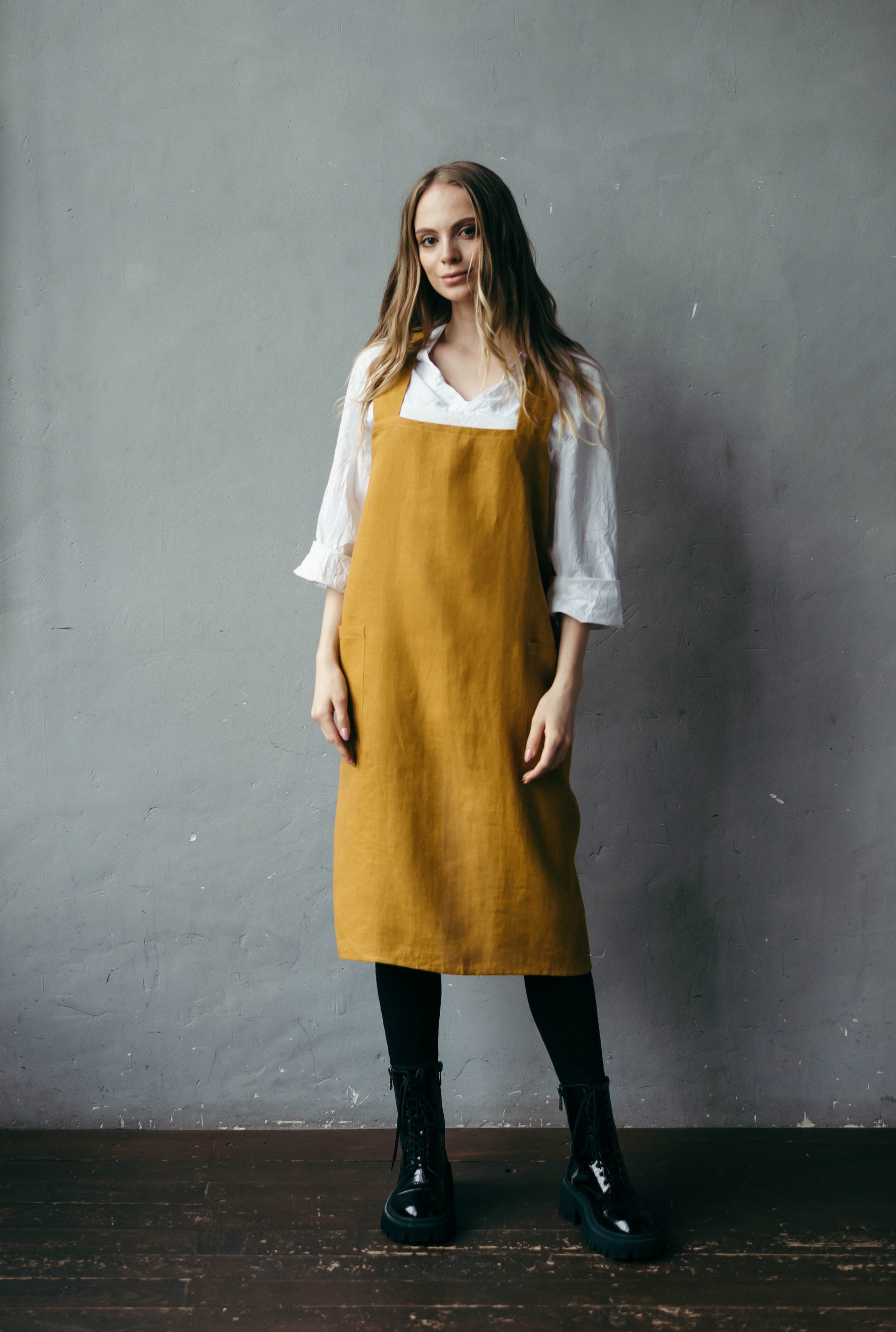 Woman wearing mustard linen pinafore apron with cross-back straps.