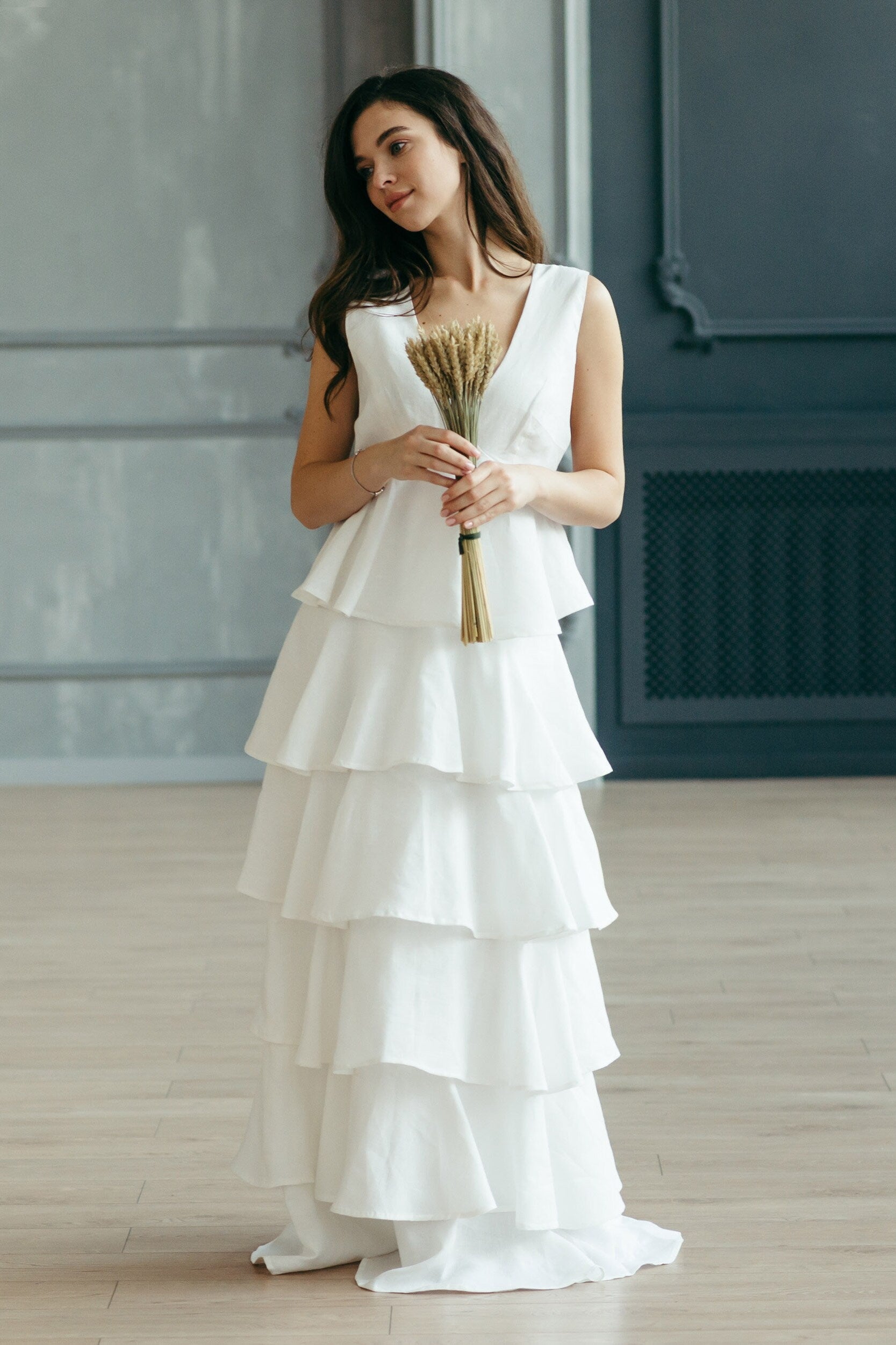 Bride in a white boho linen wedding dress holding a bouquet indoors.