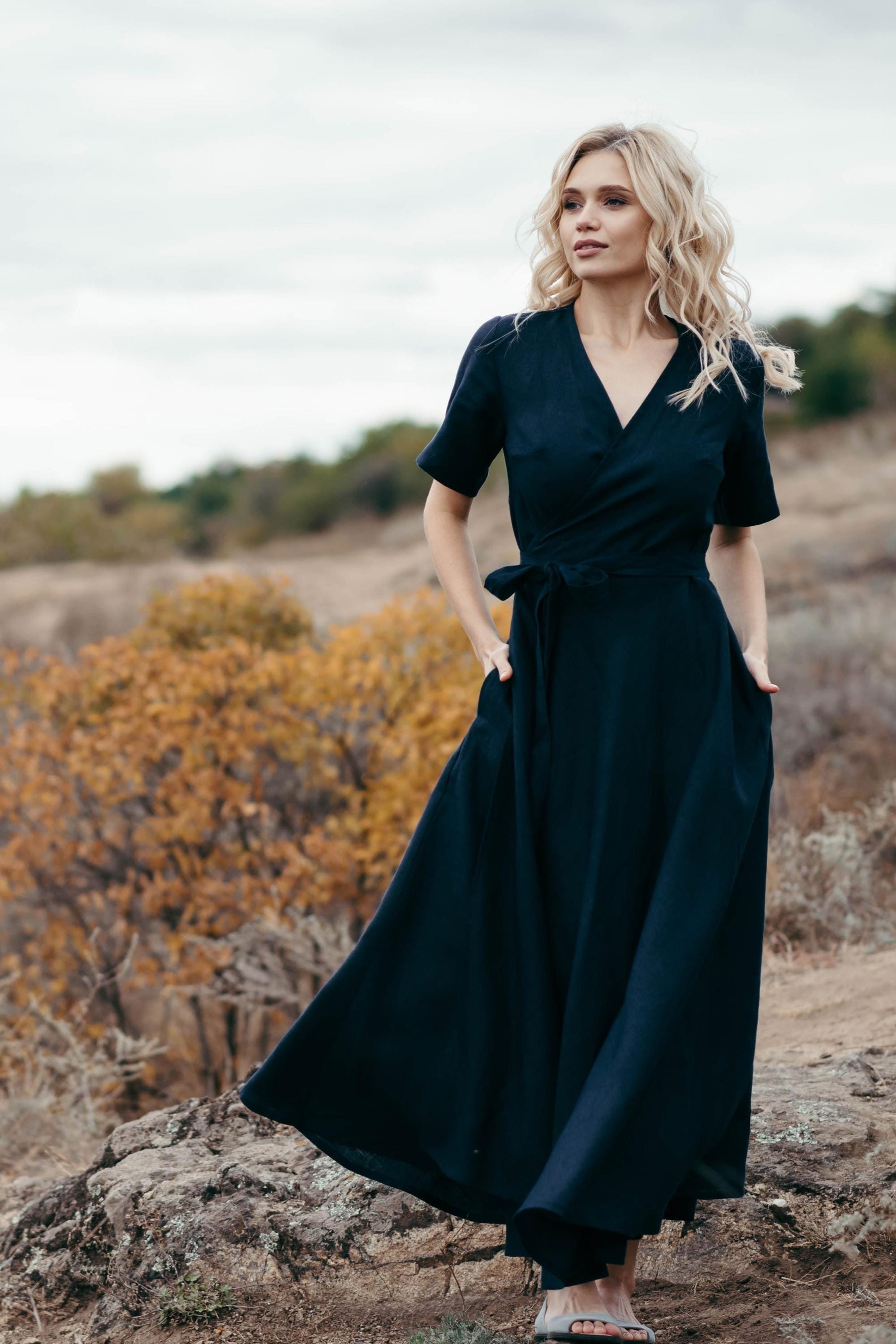 Woman in a navy blue linen dress standing on a rocky landscape with trees in the background