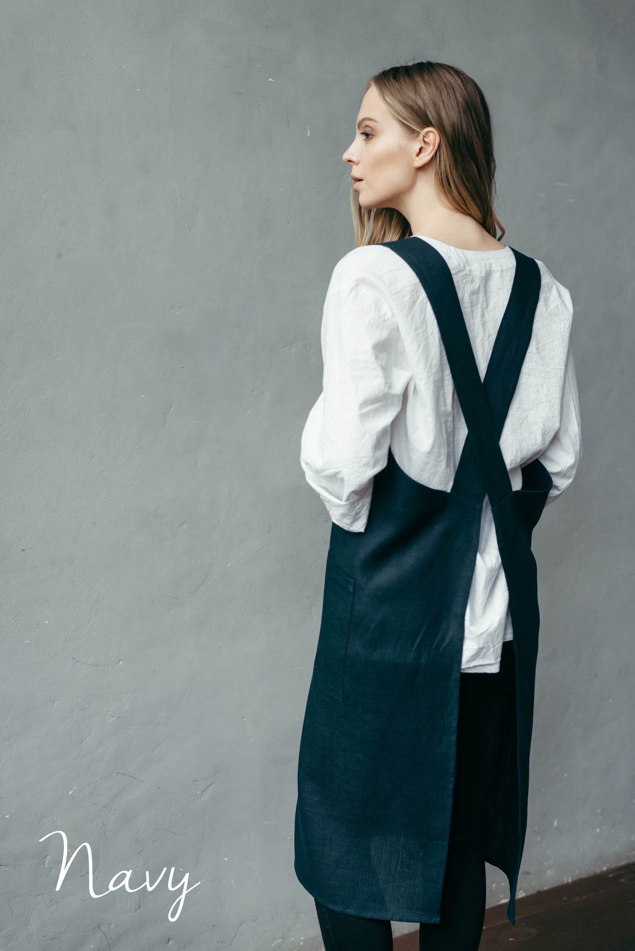 Artist wearing a navy pullover apron over a white shirt in her ceramics studio.