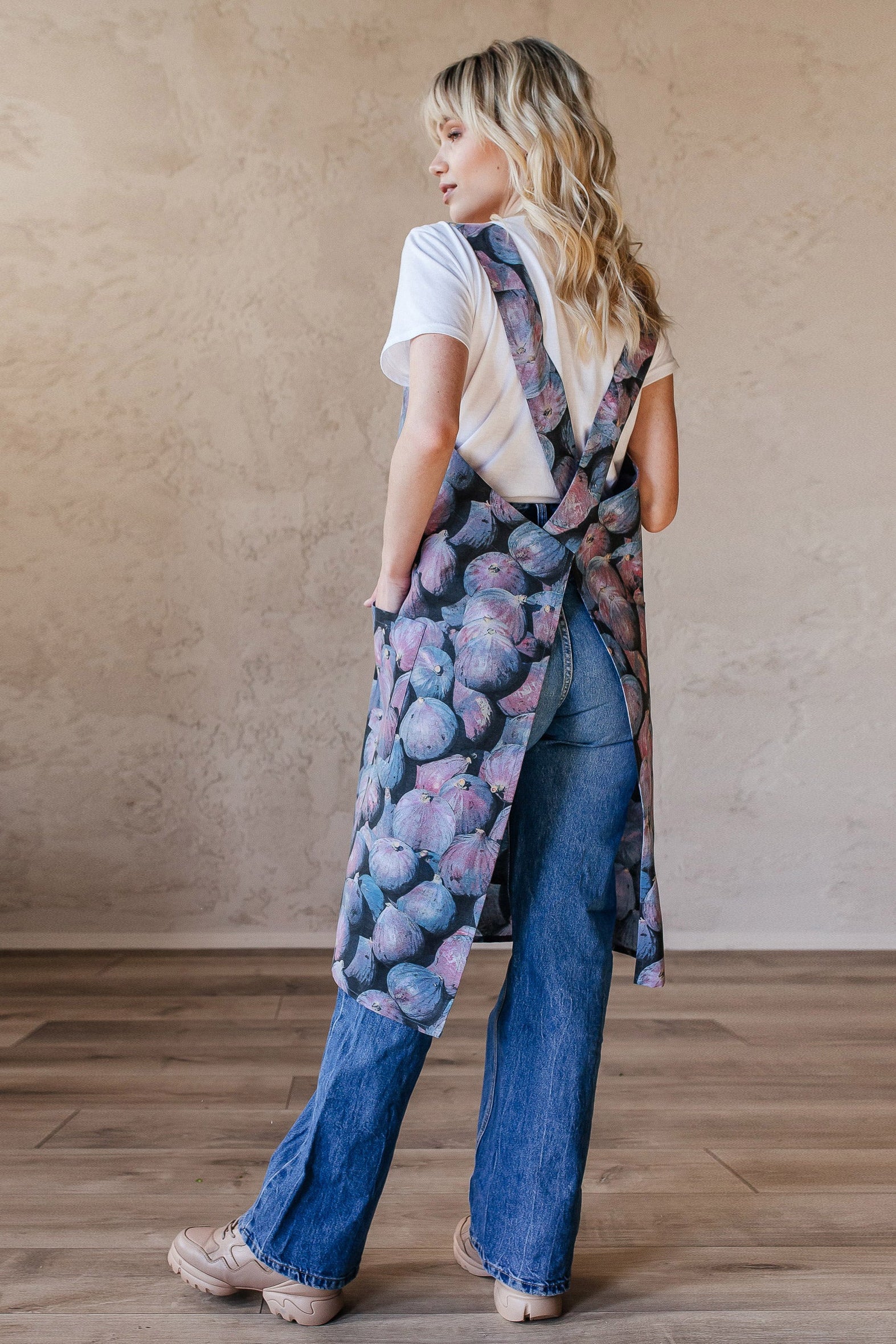 Woman wearing a cotton canvas apron over a white shirt and jeans in a minimalistic room.