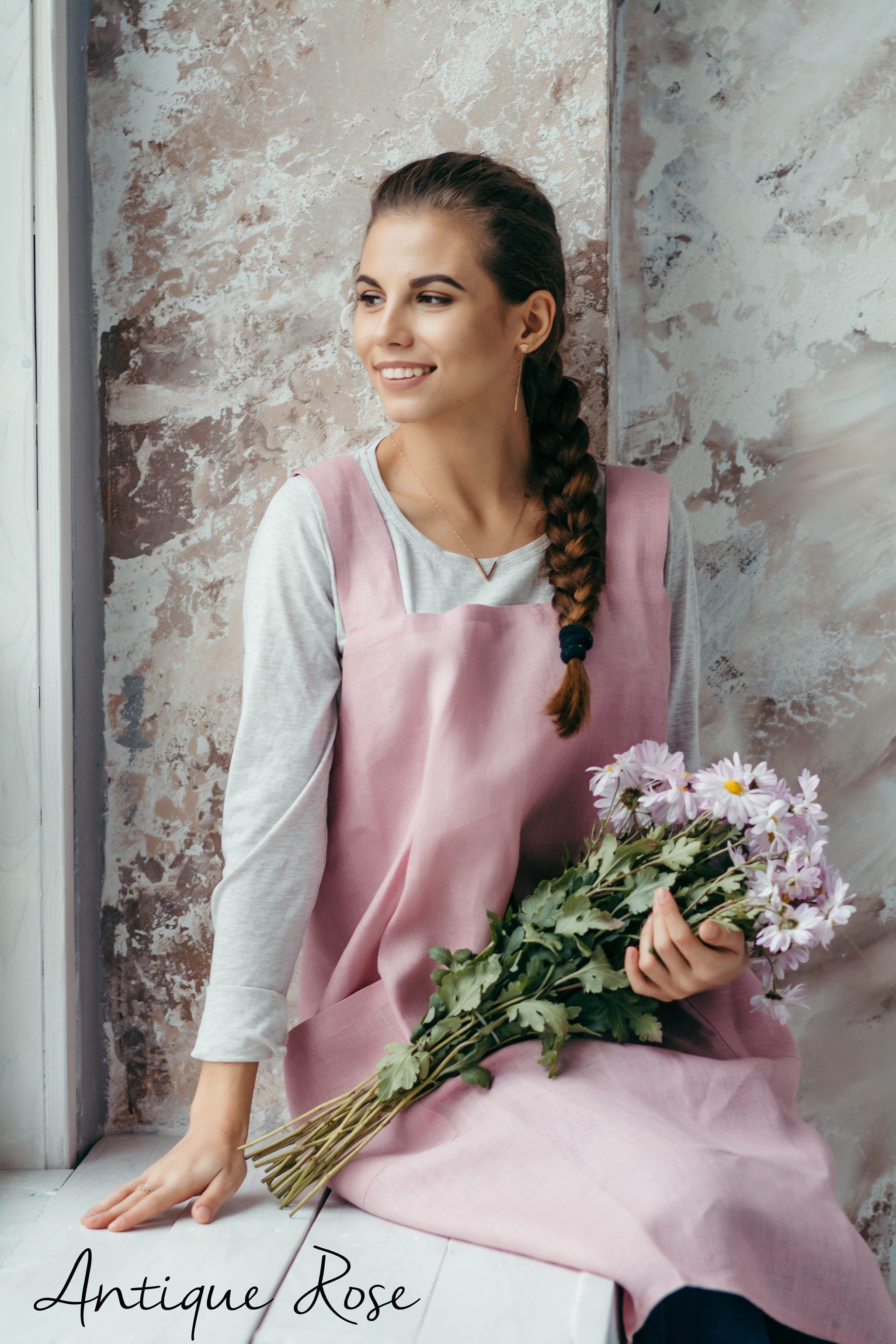 Florist in a pink linen apron holding flowers against a textured wall.